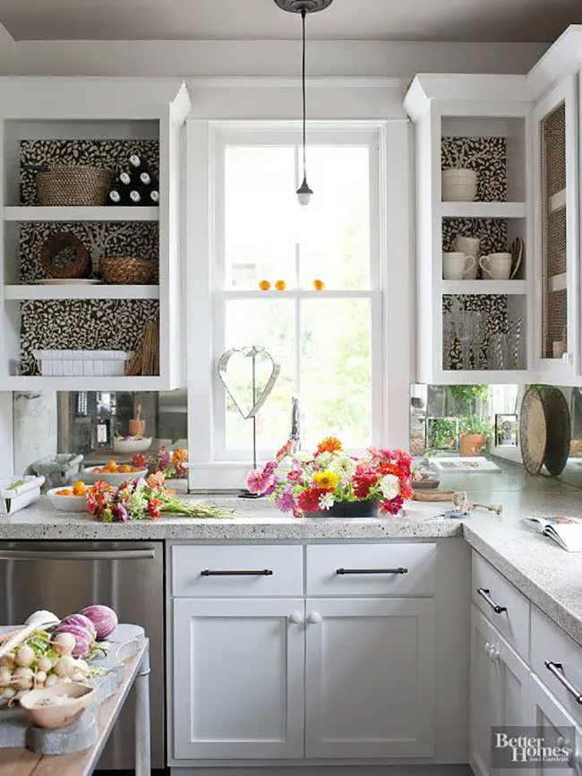 Putting black and white patterned wallpaper behind the shelves creates a really cool look. It makes the simple white cups and bowls stand out clearly against the busy background. This is a very artistic no door kitchen cabinet idea that adds texture to the room.