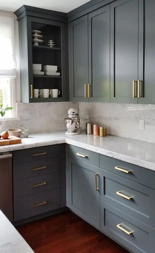 Dark gray cabinets create a sleek and modern look in this corner kitchen. Removing the door from the upper corner cabinet provides a perfect spot to display white mugs and bowls. This simple change breaks up the solid block of color and adds depth.