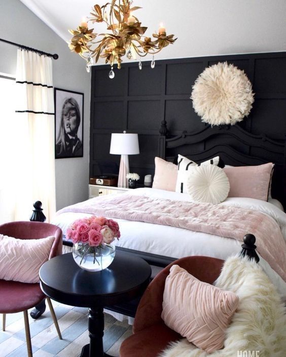 A wall of black panels adds a lot of texture behind the bed. The big white feather decoration and the gold light fixture look amazing together in this cozy pink and black bedroom.