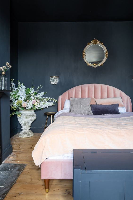 The matte black wall really makes the pink velvet headboard pop. A large stone vase filled with flowers adds a romantic touch. This pink and black bedroom feels very soft and elegant.