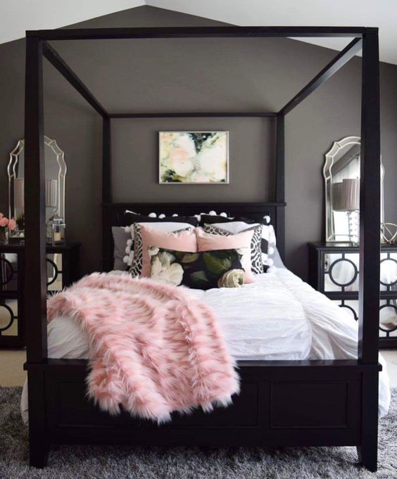 Mirrored nightstands add a lot of sparkle next to the tall black bed frame. The large floral painting brings all the colors together. This pink and black bedroom looks very comfortable with that big fur throw.