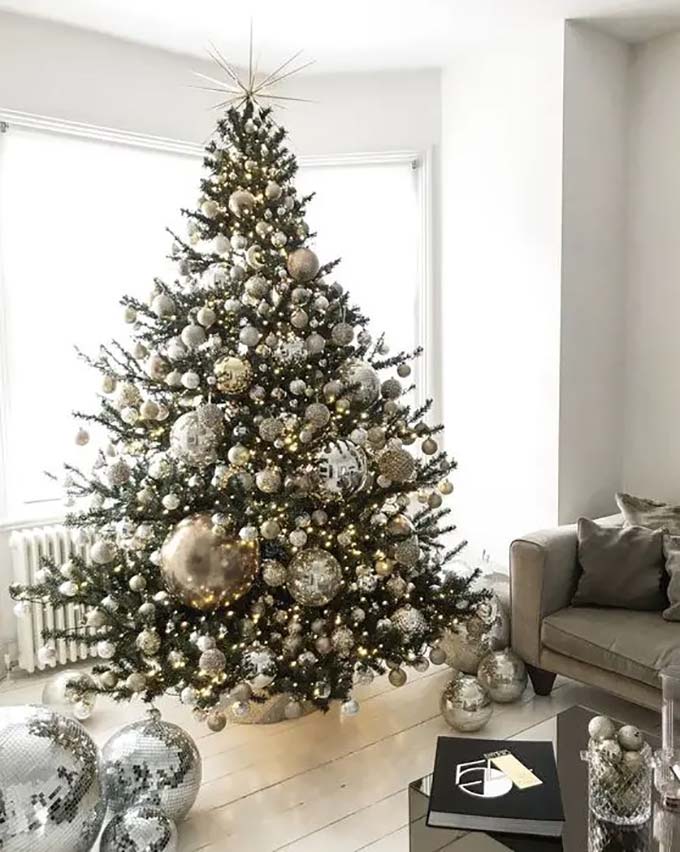 This tree is packed with shiny silver and gold balls. There are even big, sparkling silver disco balls on the floor next to it!