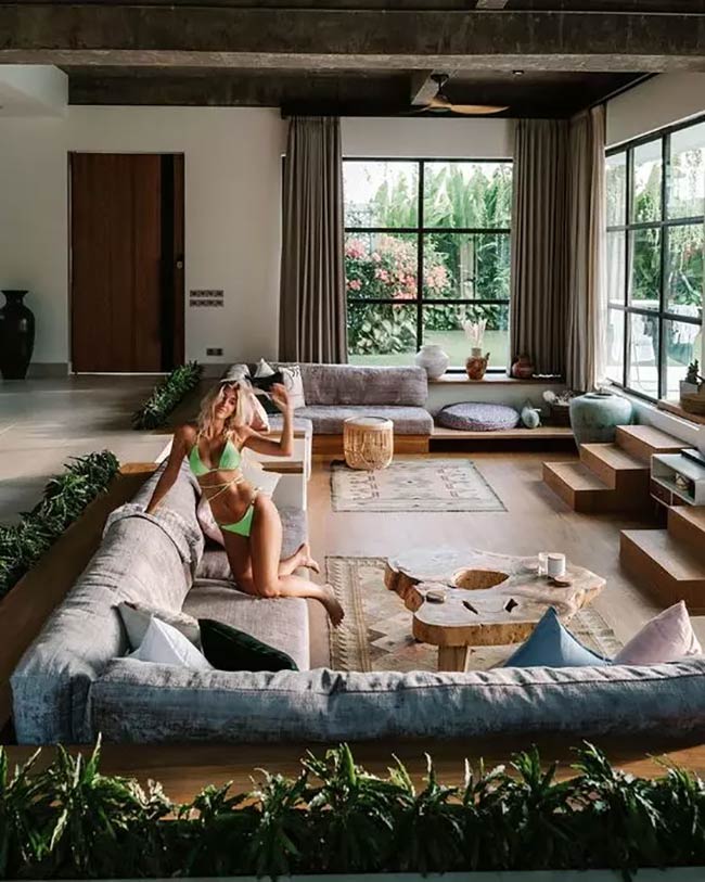 Plants are growing all around the edge of this sunken sofa. The big, natural wood table is very cool. This looks like a very relaxing conversation pit.