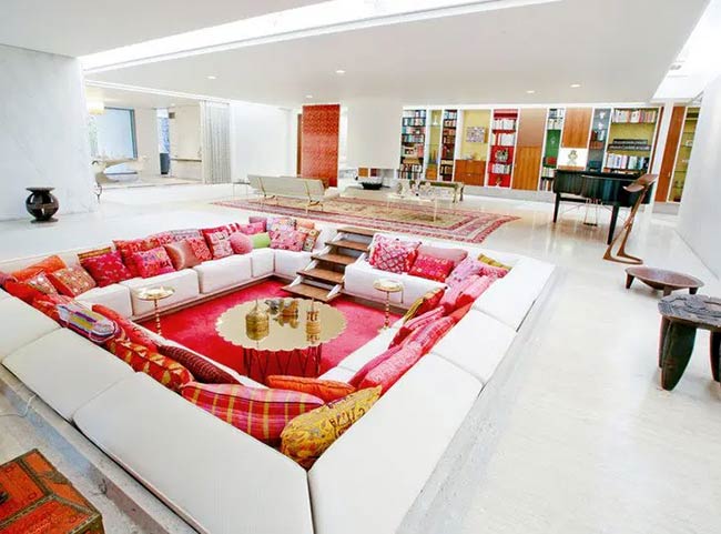 What a colorful conversation pit! The white sofa is covered in bright red and pink pillows. A red rug and gold table sit in the middle of the huge sunken area.