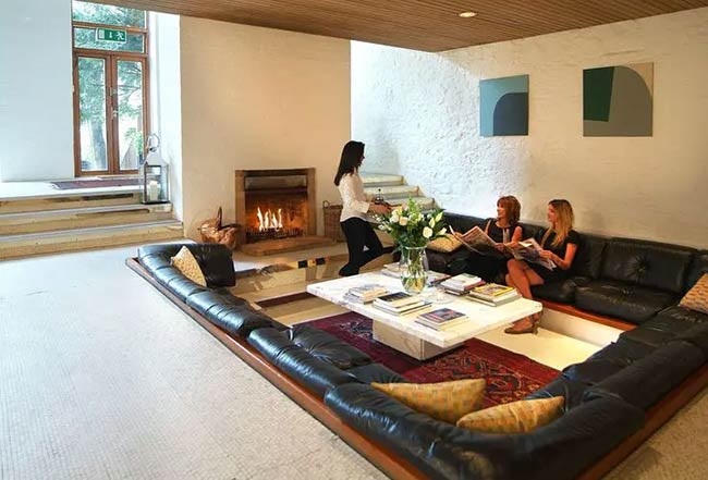 A huge, black leather sofa lines this sunken living room where people are relaxing by the fireplace.