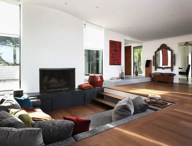 This long, gray sunken sofa is built right into the wooden floor, sitting across from a fireplace.