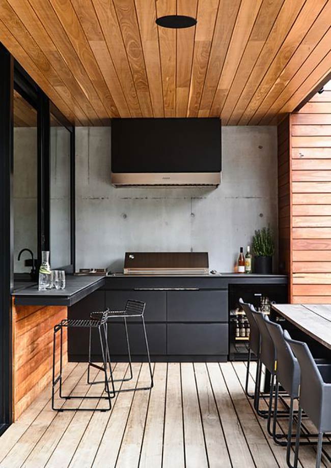 Matte black cabinets against the smooth concrete wall look incredibly modern and cool. The wood ceiling warms up the dark colors of this outdoor barbeque area. A small wine fridge tucked under the counter is a great bonus for parties.