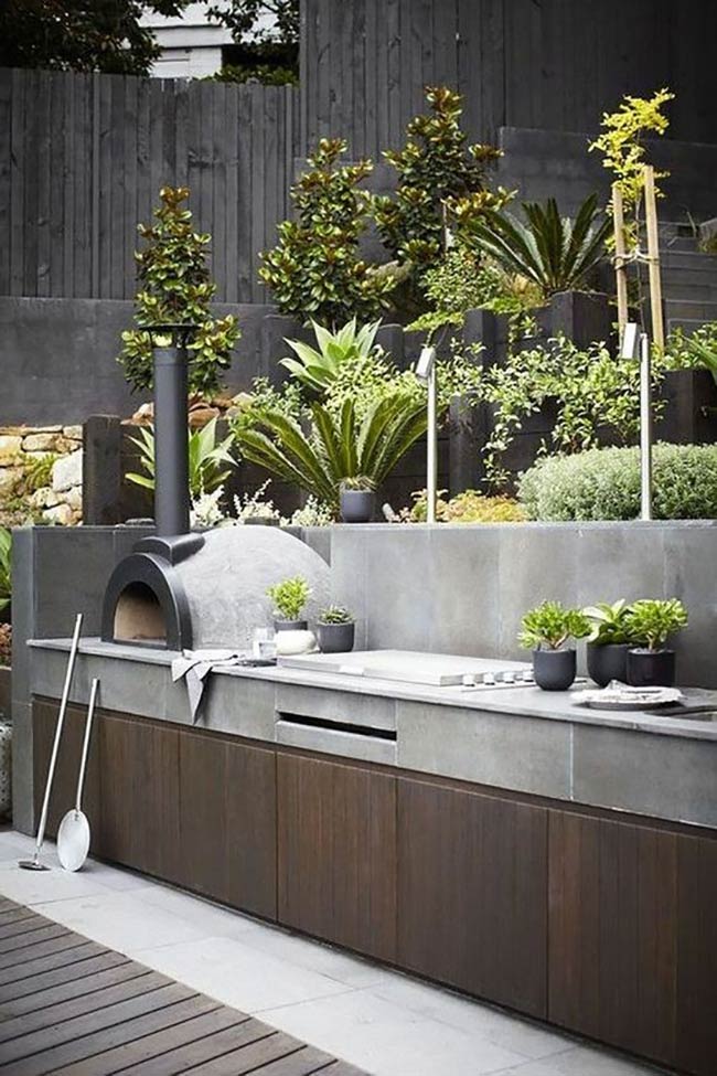 The black pizza oven is the star of this modern outdoor barbeque area. Sleek concrete countertops sit above dark wood cabinets for a stylish contrast. It looks like a perfect place to make dinner in the garden.