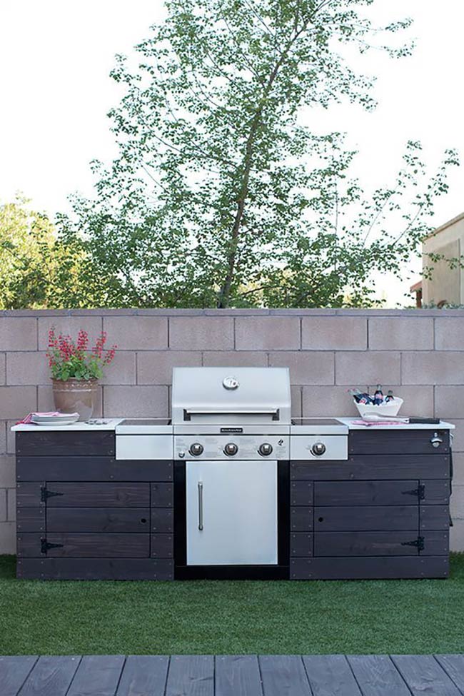 Dark stained wood planks give this grill station a unique and bold look against the light wall. The white countertop provides a clean space for prepping food next to the barbecue.