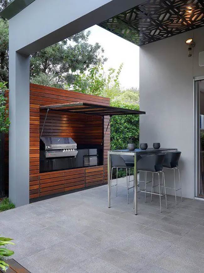 Tucked into a modern wood niche, this grill station saves a ton of space. The fold-up door protects the cooking area when it's not in use, keeping everything clean. A sleek high table nearby is perfect for quick meals.