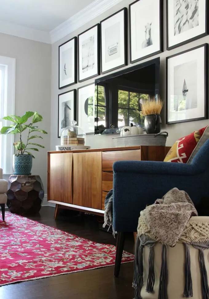Rows of matching black frames hang high above the television to draw the eye upward. The wooden cabinet hides wires and adds warmth to the simple gray wall.