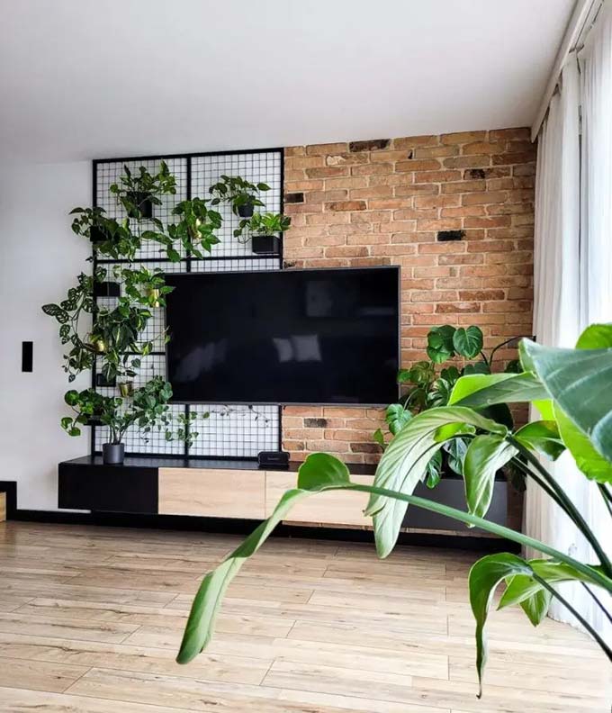 Half of the wall is old red brick, while the other half features a black metal grid. Real green plants climb up the grid next to the flat screen for a unique living wall look.