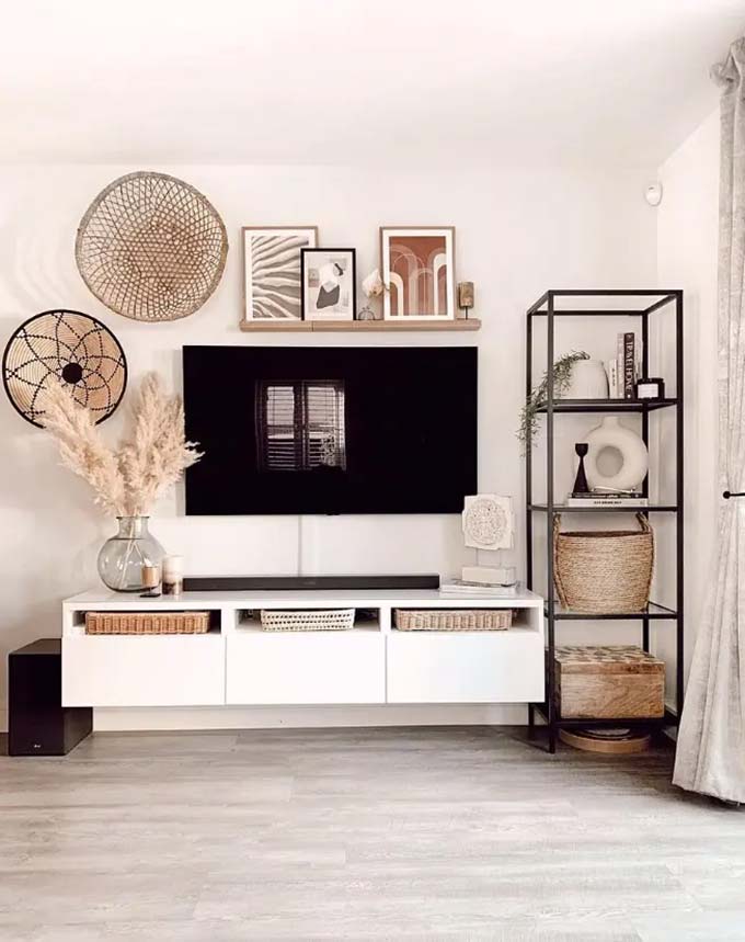Round woven baskets hang on the wall to add texture above the screen. A simple white cabinet floats off the floor to keep the look clean and open. This boho TV wall decor style uses dried plants and wood for a soft, natural touch.
