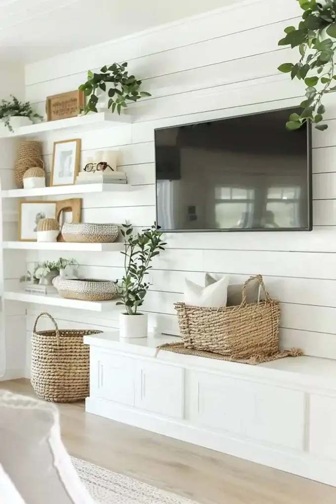 Building shelves on both sides of the fireplace makes the TV look like it belongs there. The white shiplap walls and neutral colors create a very calm and soft living room atmosphere. It is a classic TV wall decor layout that offers plenty of space to display beautiful objects.