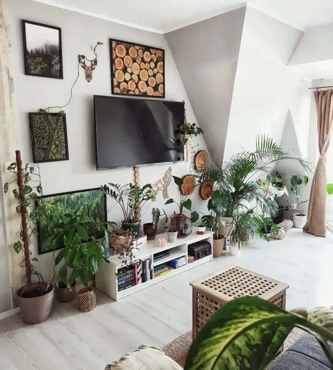 A deep blue wall makes the vintage wooden cabinet and art frames stand out clearly. Many small pictures are arranged around the TV to create a collected and cozy gallery look. This TV wall decor style feels very personal and retro with the wicker furniture.