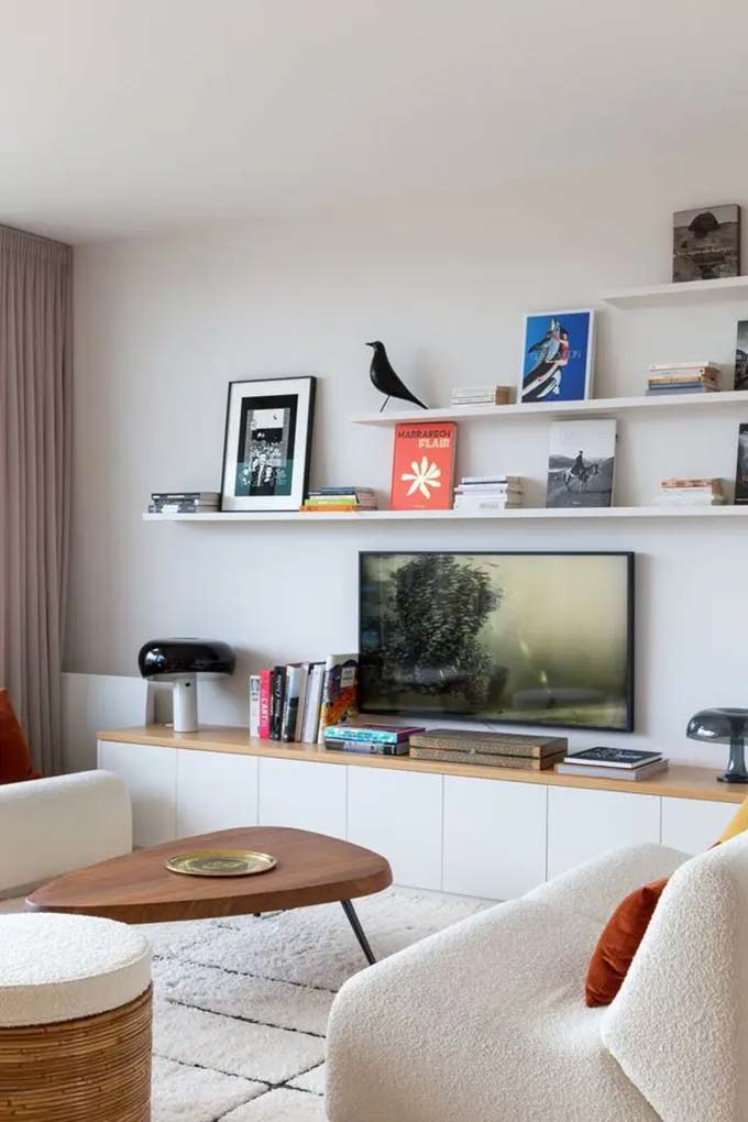 A soft blue wall creates a pretty background for a mix of art frames and woven baskets. The white cabinet with gold starbursts adds a fancy touch under the screen. This fun TV wall decor setup feels very relaxed with the texture of the round floor poufs.