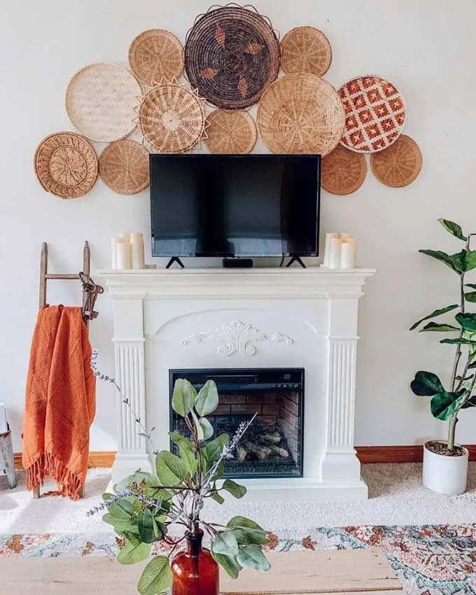Hanging many round baskets in an arch shape draws attention away from the black screen. Placing the TV on a classic white mantel saves space in the living room. This boho TV wall decor idea adds a nice warm texture to the plain white wall.
