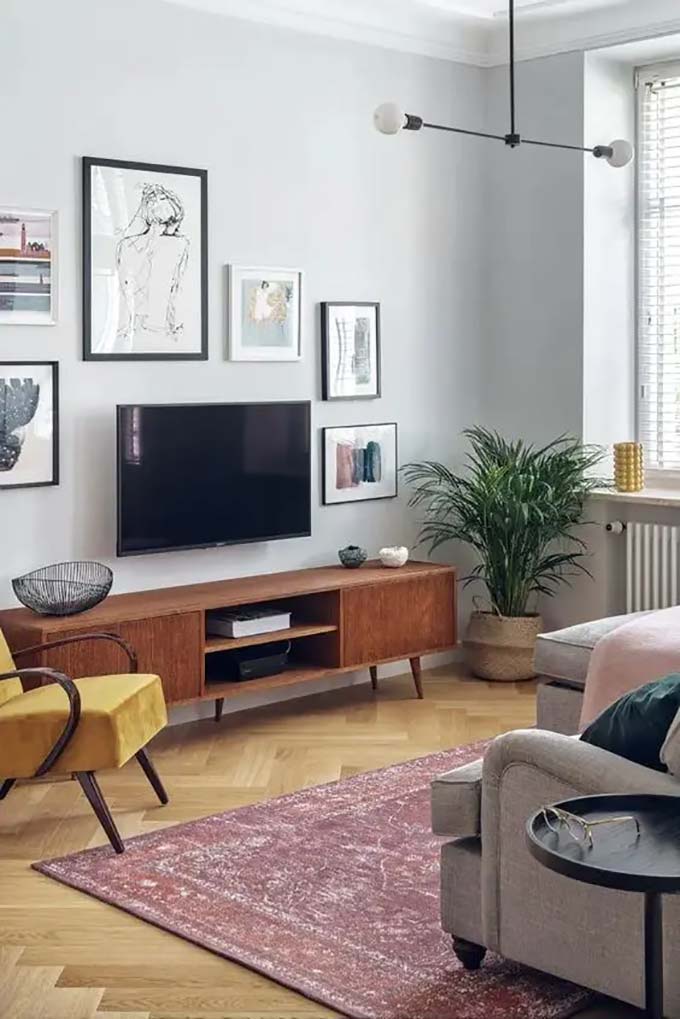 Bright orange shelves add a fun splash of color high above the screen. The room feels like a real jungle with huge green plants surrounding the entertainment area. This lively TV wall decor brings nature right inside the home for a fresh look.