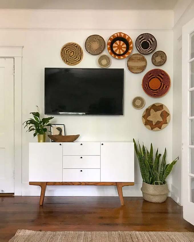 Long white floating shelves create clean horizontal lines across the wall. Leaning art prints and books on the shelves makes the space feel casual but organized. It is a very modern and bright TV wall decor choice for a minimalist home.