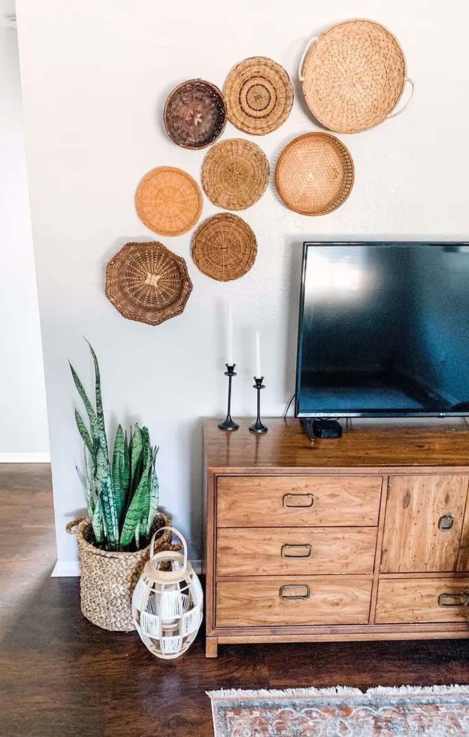 Arranging round woven baskets in a curved shape creates a lovely focal point above the television. The different shades of brown match the vintage wooden dresser perfectly. This simple TV wall decor idea brings a warm and handmade feel to the room without needing expensive art.