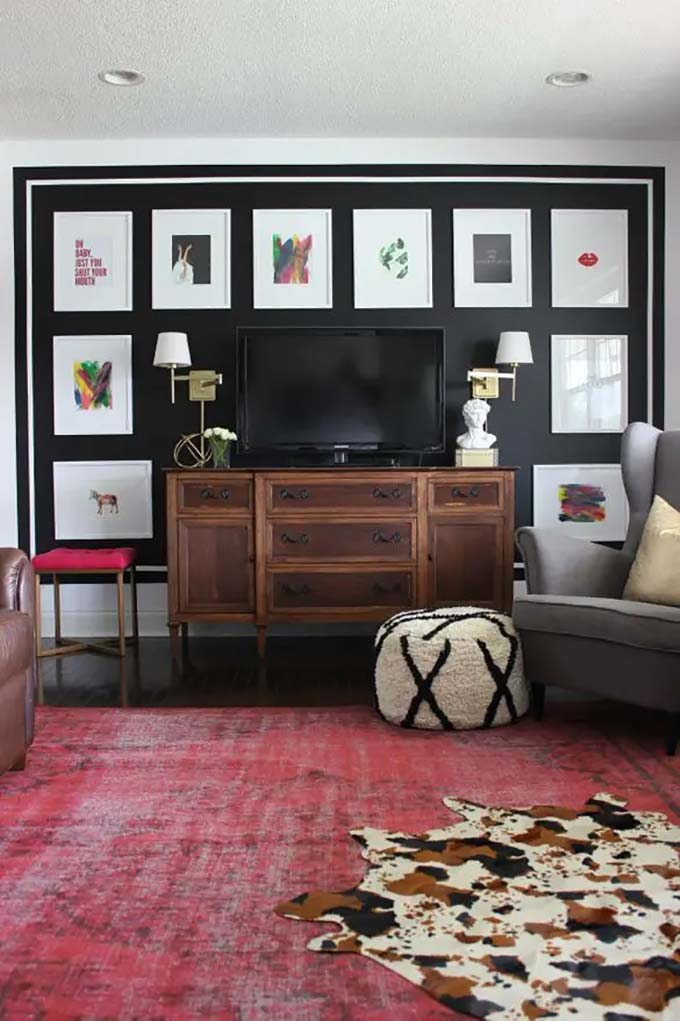 Painting the wall black makes the matching white picture frames pop out brilliantly. A neat grid layout surrounds the screen to keep everything looking organized and fancy. The bright red rug on the floor adds a fun splash of color to this bold TV wall decor.