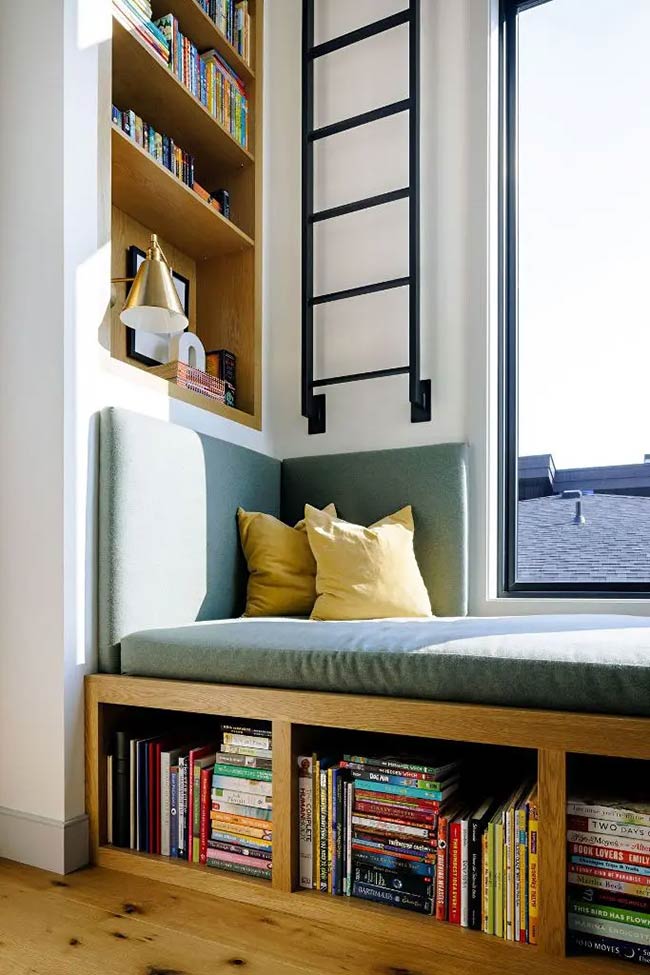 This reading nook uses every inch of vertical space with tall shelves and a black library ladder. The green cushion creates a cozy place to sit, while open cubbies below provide easy under window storage for even more books.