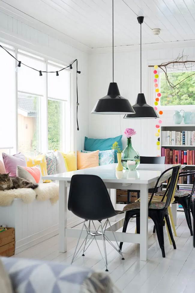 A long white bench filled with colorful pillows replaces traditional dining chairs. You can hide wooden crates underneath for extra under window storage. It creates a fun and casual atmosphere for eating family meals.