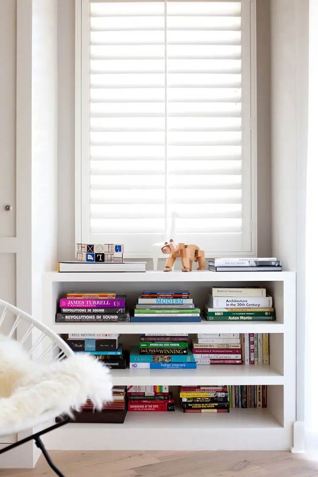The white plantation shutters control the light beautifully in this small alcove. Built-in shelves below the window keep colorful books organized and ready to read. It is a neat and tidy under window storage solution for a small collection.