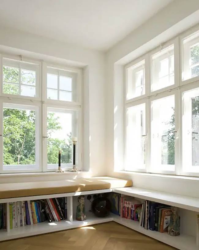 This custom white bookshelf wraps perfectly around the corner to make use of every inch. The long yellow cushion provides a sunny and comfortable place to sit and read. It is a fantastic under window storage idea for creating a mini library with a view.