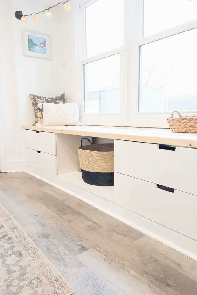 Clean white drawers and a light wood top give this bench a fresh and modern look. The open cubby in the middle is perfect for holding a large woven basket. This simple under window storage design keeps the hallway feeling bright and organized.