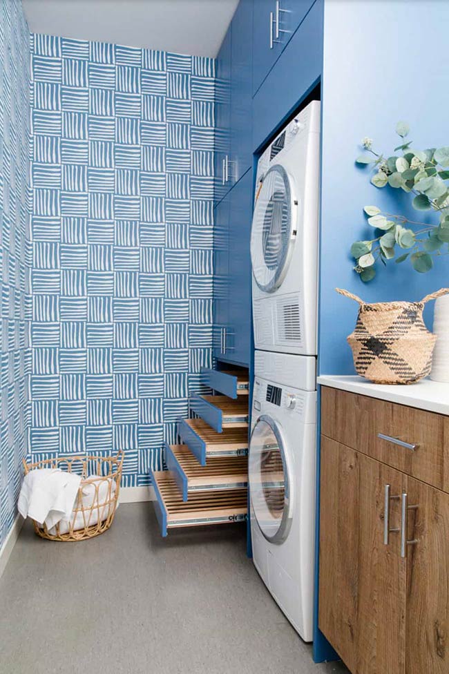 Revel Blue cabinets and playful wall coverings make this laundry room lively. Pull-out drying racks and basket rollouts keep items organized and easy to access. Functional design meets color energy, turning laundry chores into a more enjoyable task.