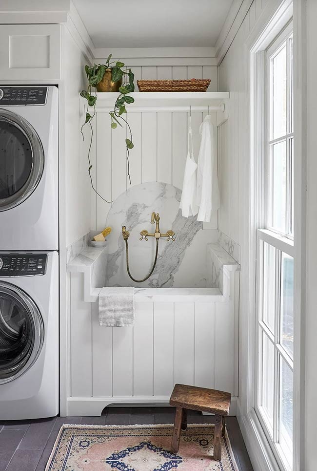 This laundry room combines function and beauty effortlessly. Stackable Electrolux appliances sit next to a marble-effect utility sink. Custom cabinets offer plenty of storage, and terra cotta floors add warmth and texture. Neutral paint and soft white cabinetry keep the space fresh and timeless. This is a perfect example of a laundry room that is not just functional, but also visually appealing.